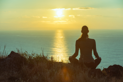 Mujer meditando frente a una puesta de sol